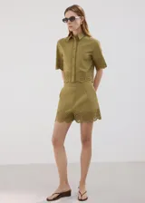 Camisa crop de algodón color verde militar, con cuello camisero, manga corta y cierre frontal con botones. Presenta detalles bordados calados y terminaciones festoneadas en el ruedo y las mangas.
