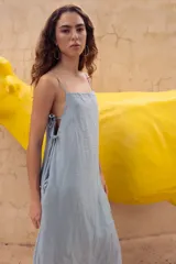 Vestido largo hasta el tobillo color celeste, de tejido arrugado liviano, con escote recto y breteles finos. Presenta lazos en los costados, forro hasta arriba de las rodillas y caída posterior más larga.