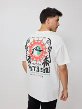 Remera blanca de algodón con estampado en la espalda que incluye un sol con un surfista en el centro, texto y motivos playeros.