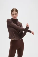 Campera deportiva de ajuste entallado, confeccionada en poliéster color gris oscuro. Presenta cuello alto, cierre frontal completo y mangas largas con aberturas para los pulgares.