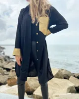 Camisola negra larga de lino con cuello camisero, cierre frontal con botones dorados, bolsillo de cuero dorado en el pecho y puños con detalle de cuero dorado.