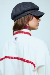 Camisa blanca de algodón con detalles de puntilla roja en cuello, solapa frontal, bolsillo y puños. Presenta botones en color celeste.