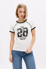 Remera de algodón blanca de manga corta estilo ringer, con cuello y puños en contraste negro. Presenta un estampado frontal con el número '28' relleno de encaje y la inscripción 'San Francisco Sports Club'.