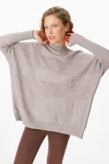 Sweater holgado de punto color beige, con cuello alto y mangas largas con puños acanalados extendidos hasta el codo. Presenta un diseño de paneles horizontales con textura sutil.