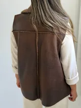 Chaleco de cuero sintético color marrón chocolate, con interior y solapas amplias de corderito sintético al tono. Diseño sin cierre y corte recto.