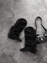 Botas altas de gamuza con flecos colgantes a lo largo del lateral, diseño slouchy y puntera fina.