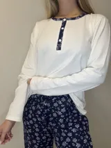 Pijama de algodón compuesto por una remera blanca de manga larga con cuello redondo, botones frontales y ribete con detalle estampado, acompañado de un pantalón azul marino con estampado floral y cordón ajustable en la cintura.