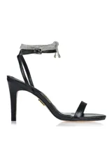 Sandalia de tacón alto color negro, con tira delgada sobre los dedos y pulsera al tobillo con hebilla y detalle de strass.