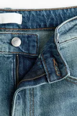 Jean de tiro alto y corte bootcut, confeccionado en denim de algodón levemente elástico con lavado azul medio y efecto desgastado. Presenta diseño clásico de cinco bolsillos, cierre de cremallera y botón metálico.