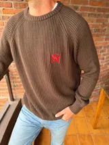 Sweater de tejido de punto acanalado en color marrón, con cuello redondo, mangas largas y bordado distintivo en color rojo en el pecho.