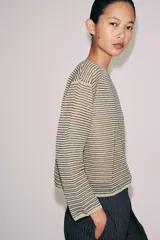 Sweater de punto fino color beige con finas rayas horizontales negras, cuello redondo y manga larga.