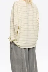 Remera de manga larga color crema con finas rayas horizontales grises. Presenta un estampado frontal grande en tonos grises y negros con tipografía y figura abstracta.