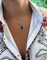 Collar con cadena de eslabones tipo caja plateada y un dije rectangular con borde plateado y centro de piedra negra pulida.