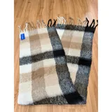 Bufanda rectangular de tejido grueso con diseño de cuadros en tonos azul, naranja, gris y beige, terminada con flecos en los extremos.