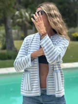Chaqueta corta tejida a rayas horizontales celestes y blancas, con cuello redondo, bolsillos frontales y ribete celeste en los bordes.