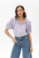 Camisa de lino color lila con volados en el cuello y en las mangas cortas abullonadas. Presenta un diseño de corte recto con cierre frontal de botones.