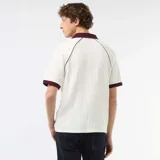 Remera de tejido de punto color blanco con cuello en V y cuello polo en contraste bordó, al igual que los ribetes en los puños y las costuras de las mangas raglán.