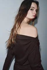 Vestido largo de color marrón oscuro, con cuello fluido tipo bote, manga larga y detalle de fruncido lateral con broche metálico en la cintura.
