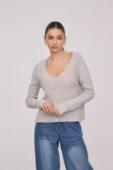 Sweater de tejido de punto fino, color beige, con escote en V profundo y mangas largas. Presenta un corte holgado y diseño minimalista.