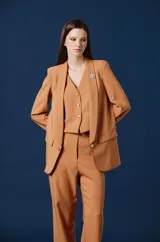 Saco de mujer con solapas clásicas, cierre frontal de un botón y bolsillos laterales con solapa. Presenta una silueta estructurada y elegante en color tostado.