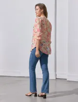Blusa de gasa estampada con flores en tonos rosa, amarillo y azul. Tiene cuello a la base, escote en V y botones. La delantera tiene detalle plisado y las mangas son 3/4 regulables con presilla y botón.
