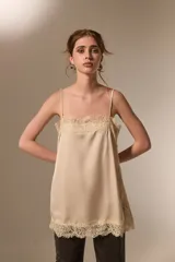 Top de tirantes finos color beige, confeccionado en poliamida con acabado satinado. Presenta un diseño recto con detalles de encaje en el escote y en el ruedo.