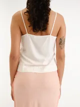 Blusa blanca sin mangas, confeccionada en tela ligera y fluida, con escote redondo y tirantes finos.