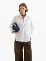 Camisa de poplin color blanco, con cuello clásico, cierre frontal de botones y mangas largas con puños. Presenta un diseño bordado de pequeñas llamas distribuidas por toda la prenda.