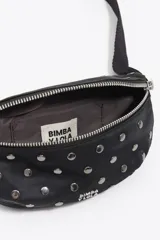 Riñonera de estructura blanda confeccionada en nylon negro, con tachas metálicas circulares en el frente. Presenta cierre de cremallera, asa regulable que combina tejido y cadena metálica, y logo de la marca estampado en la parte inferior.