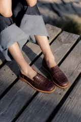 Mocasines de cuero marrón con textura efecto cocodrilo, diseño clásico de punta redondeada y suela plana con borde en tono madera.
