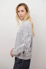 Buzo de punto color beige con cuello redondo, mangas largas con flecos decorativos y diseño de trenzas en el frente.