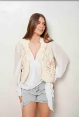 Chaleco blanco de corte corto, con bordados florales en tono tostado en la parte delantera.
