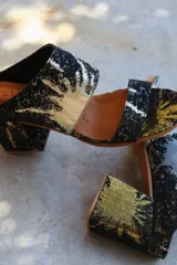 Sandalias de tacón alto con diseño de dos tiras anchas, confeccionadas en tela con estampado abstracto en tonos dorados y negros. Presentan un tacón cuadrado forrado en el mismo tejido.