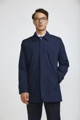 Gabardina de corte recto y estilo minimalista, color azul marino, con cuello camisero, cierre frontal oculto por solapa y puños ajustables con botón.