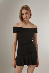 Vestido corto de poliéster color negro, con diseño ajustado al cuerpo, cuello strapless con doblez y frunces en el torso, finalizando en una falda con volados en el ruedo.