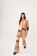 Pantalón de lino color beige, de corte flared y tiro medio alto. Presenta cierre y trabilla metálica, bordado en la pretina con hilo plata y estampado por serigrafía con figuras en marrón y negro.