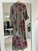 Vestido largo color visón con estampado floral en tonos fucsia y verde, de corte recto, con mangas largas arremangables, cuello camisero y cierre frontal parcial con botones.