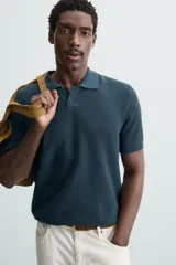 Polo de manga corta color verde azulado oscuro, confeccionado en tejido de punto con textura. Presenta cuello solapa y cierre frontal de botonadura.