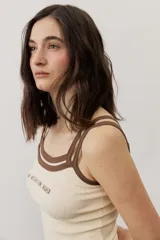 Musculosa de tejido rib color beige con detalles en marrón oscuro en el escote y doble tirante fino. Presenta un pequeño texto estampado en el pecho.