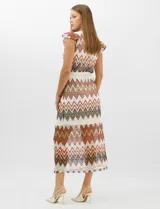Vestido midi confeccionado en tejido de punto calado, con patrón geométrico en zigzag en tonos blanco, marrón, tostado y azul. Presenta escote a la base, mangas cortas con volados en los hombros, silueta recta y forro interior a tono. Incluye un cinturón fino con hebilla metálica.