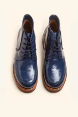 Bota acordonada de cuero vacuno con acabado charol color suela, con suela de goma tipo crepe y costuras reforzadas.