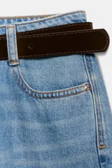 Jeans de tiro alto con pernera ancha y corte cropped. Presenta diseño de cinco bolsillos, cierre frontal con cremallera y botón, e incluye un cinturón oscuro con hebilla metálica.