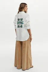 Camisa de lino blanca con detalles de bordado azul en el frente, espalda y puños, mangas largas y corte holgado.