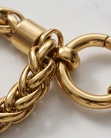 Pulsera de eslabones trenzados en acero con baño de oro, con cierre circular frontal tipo mosquetón.