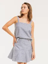 Falda corta color beige con rayas verticales blancas, corte evasé y volado en el ruedo.