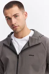 Campera con capucha y cierre frontal, color beige, con detalles de costuras y cierres en negro. Presenta mangas largas con puños acanalados y logo pequeño en el pecho.