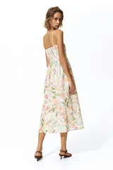 Vestido midi de color crudo con estampado floreado en tonos pastel, escote cuadrado y tirantes finos. Presenta un diseño ajustado en el torso con corte en la cintura y falda fluida con vuelo.