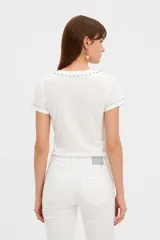 Remera negra de manga corta, con cuello redondo y ajuste al cuerpo. Cuenta con un gran estampado floral en tono gris en el frente y detalle de tachas plateadas alrededor del cuello y en los puños.