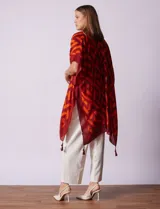 Kimono ligero de poliéster con estampado geométrico en tonos rojo oscuro y naranja. Presenta mangas anchas y terminación con borlas en los ruedos.