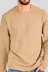 Buzo de manga larga con cuello redondo, confeccionado en tejido de punto con textura tipo waffle. Presenta un diseño minimalista con una pequeña etiqueta decorativa en el ruedo inferior.